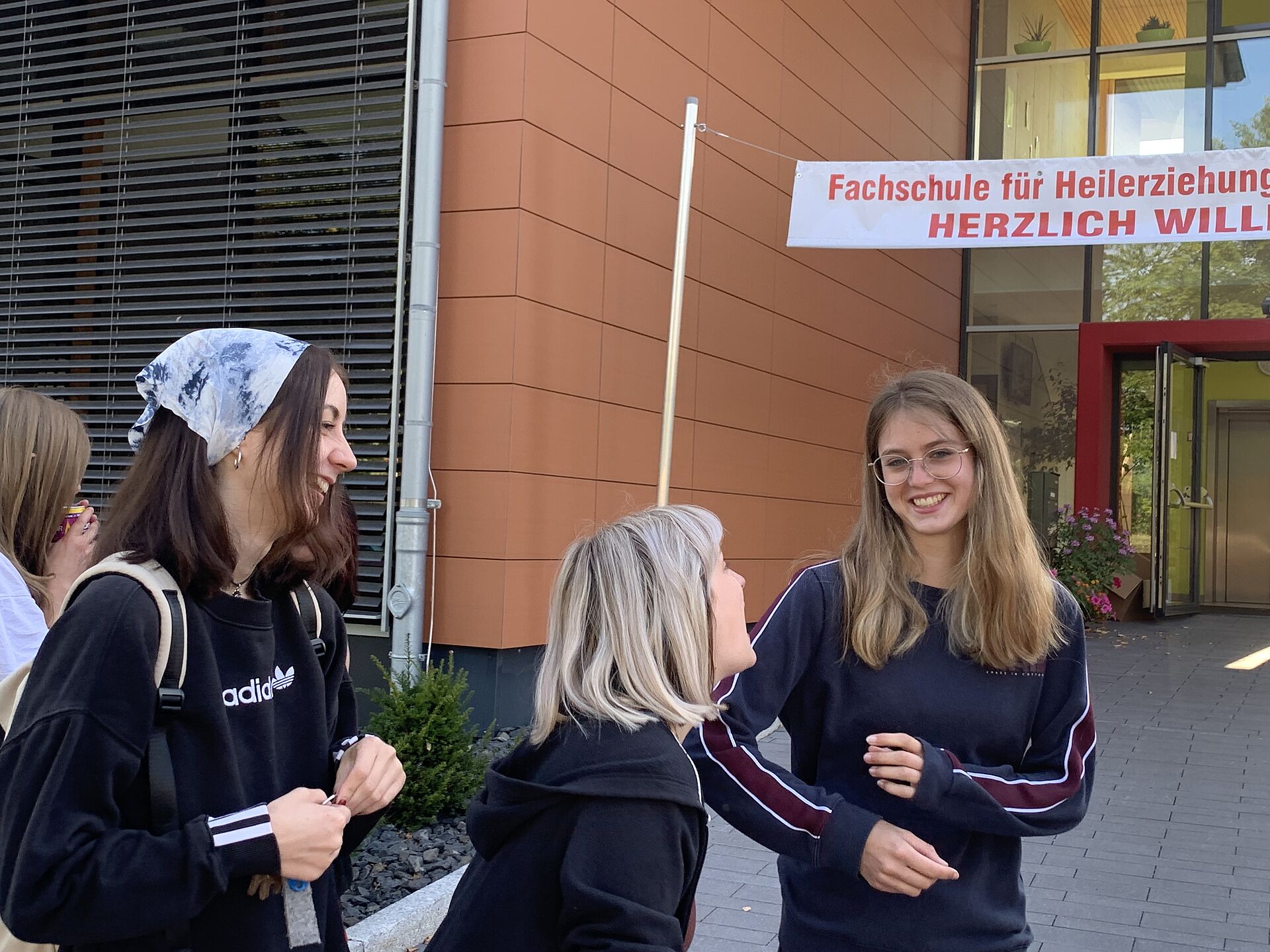 Drei Schülerinnen amüsieren sich vor der Schule, als die Lehrer examiniert werden. 